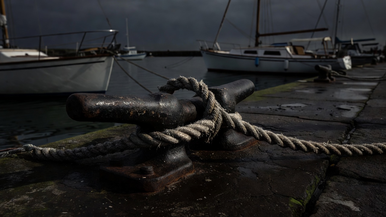 Mooring rope secured around metal harbour hardware on a shadowed quayside