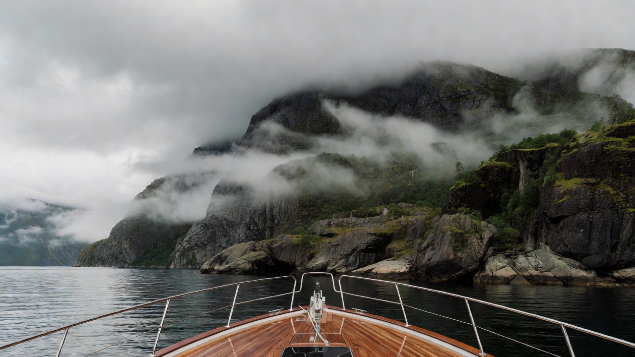 Yacht foredeck facing a steep fjord shoreline beneath low cloud